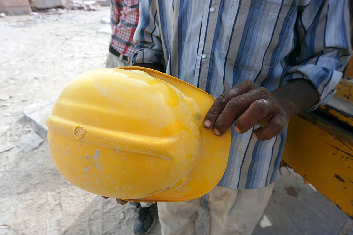 Intialainen työmies esittelee keltaista kypärää