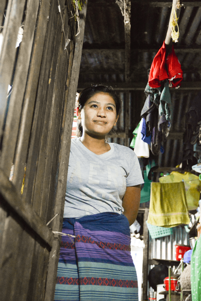 Myanmarilainen nainen seisoo vaatimattoman kotinsa ovella