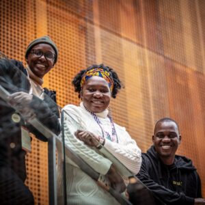 Zimbabwelaiset muusikot Chioneso Rutsito, Edith Katiji ja Luckmore Magaya nojaavat portaikon kaiteeseen ja katsovat hymyillen kameraan