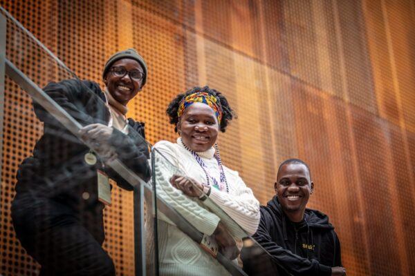 Zimbabwelaiset muusikot Chioneso Rutsito, Edith Katiji ja Luckmore Magaya nojaavat portaikon kaiteeseen ja katsovat hymyillen kameraan
