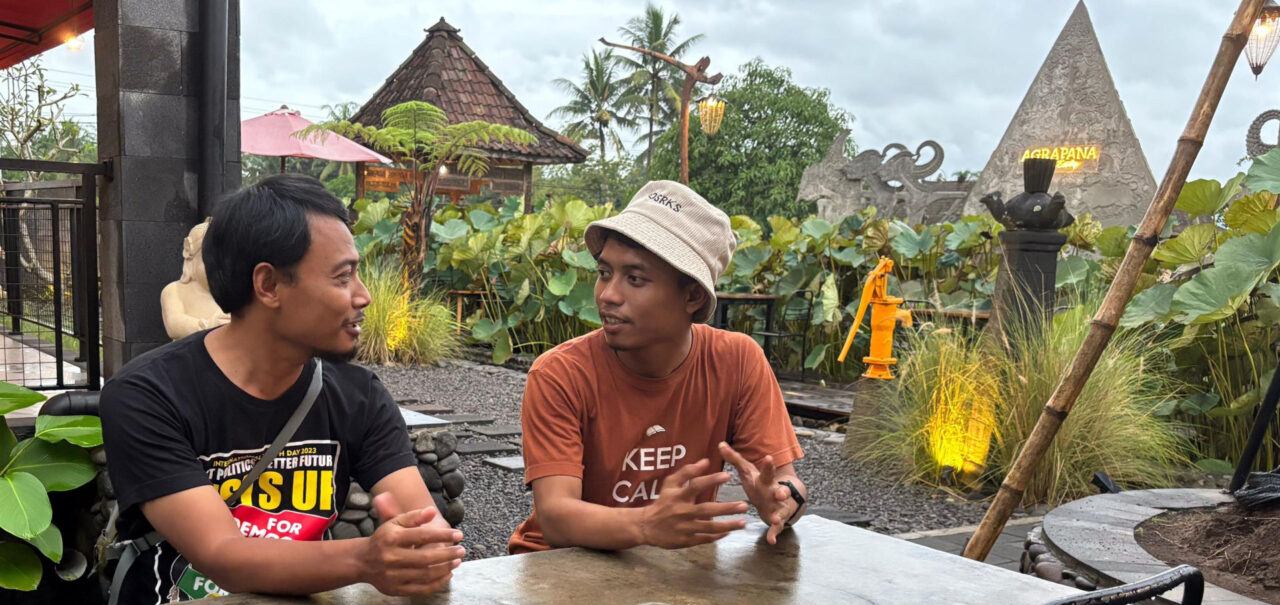 Kaksi indonesialaista miestä istuu ulkona pöydän ääressä katsoen toisiaan.