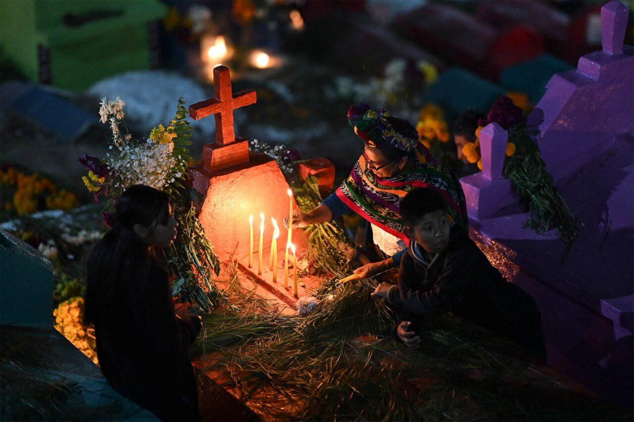 Guatemalalainen perhe sytyttää kynttilöitä omaisensa haudalle hämärsääs valaistuksessa