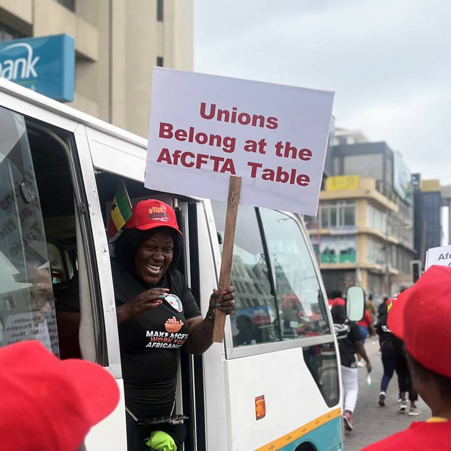 Mielenosoittajanainen Ghanassa kurkistaa bussista kädessään kyltti: Unions Belong at the AfCFTA Table